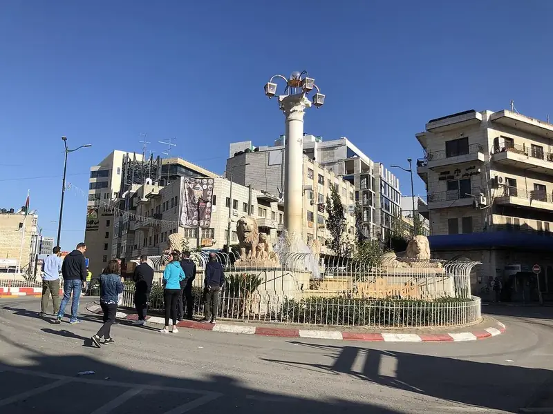People cross Al-Manara Square in Ramallah under a clear sky.